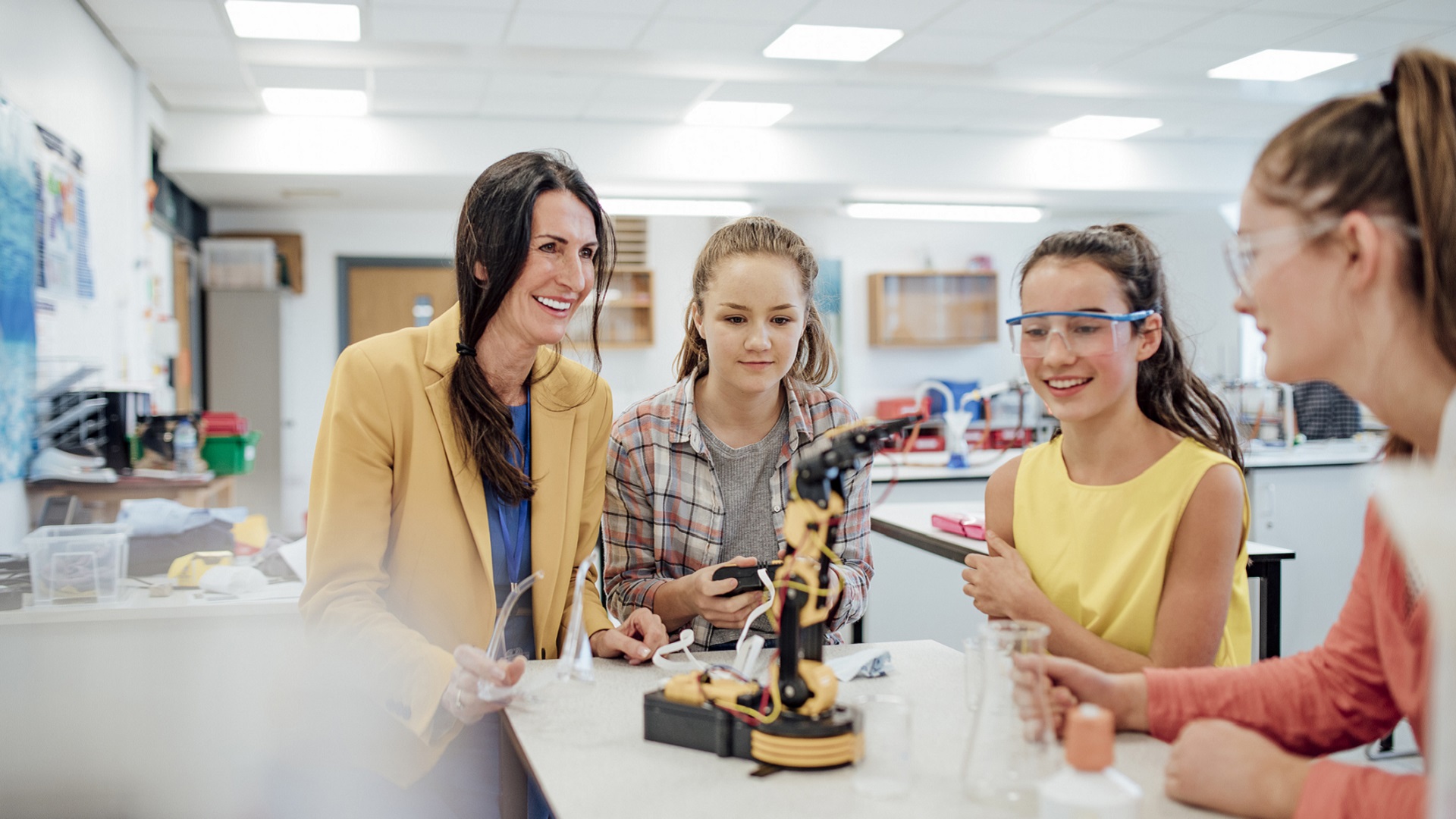 Point of view angle of teenage girls studying robotic arm in school.