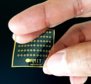 Closeup of hand holding square f clear material with gold dots and RMIT university logo