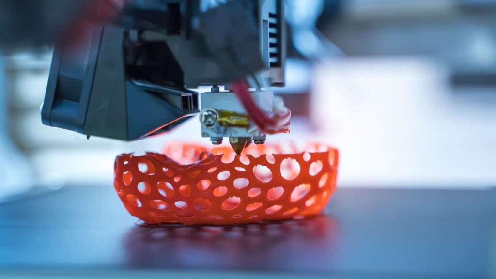 A 3D printer in action, with a curved red shape underneath.